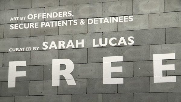 Exhibition videographer. A wall made from grey concrete blocks with white vinyl text.