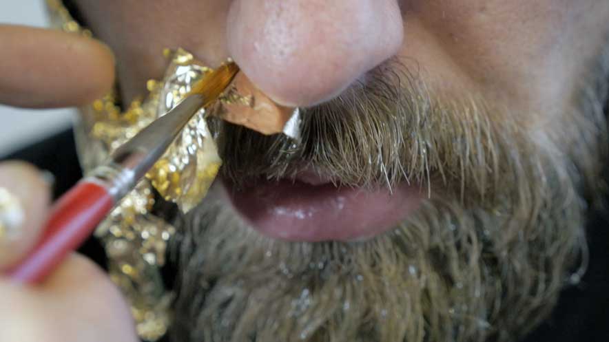 Producing a music video. Close up shot of a fine artists paint brush applying gold leaf over onto beard hair