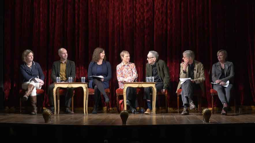 Filming a panel discussion. Seven panel guests sitting on separate chairs on stage