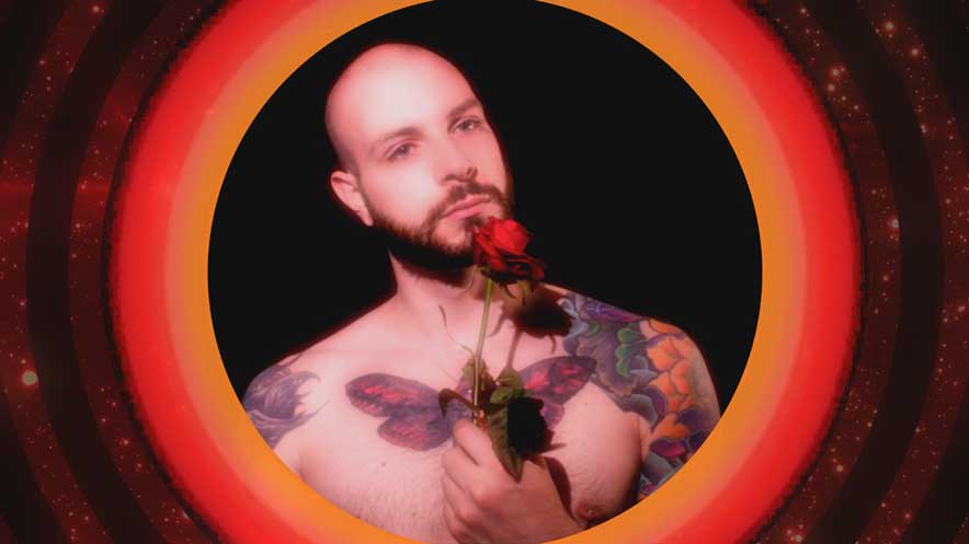 YouTube music videos. Shirtless upper torso of a man with tattoos holding a single stem red rose against a black background with an orange and red circular visuals surround.