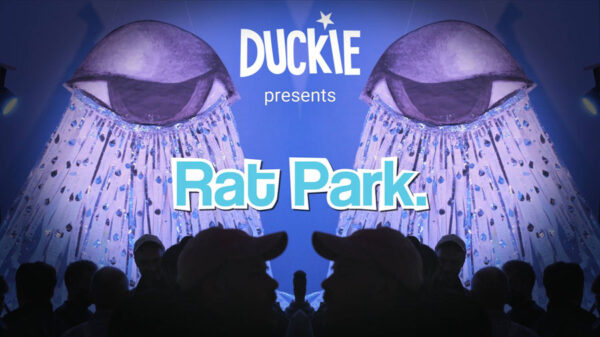 Rat Park documentary opening frame. Two artistic crying eyes hang, lit on a stage against a blue background. People in shadow look on.