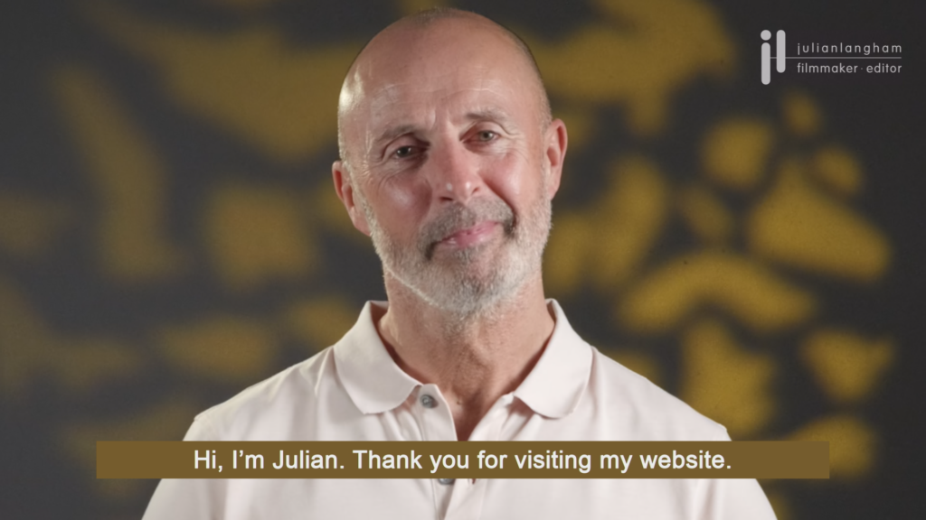 Welcome to my video production website with subtitles 16:9 version showing close up of Julian's face with a mottled grey and gold background with white text over a gold strap background.