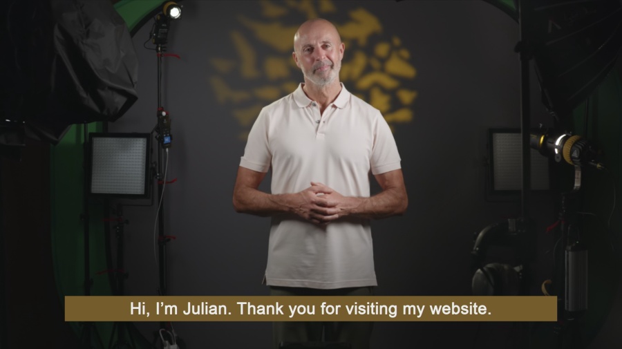 Welcome to my video production website with subtitles 16:9 version showing wide angled of Julian with lighting kit with a mottled grey and gold background with white text over a gold strap.